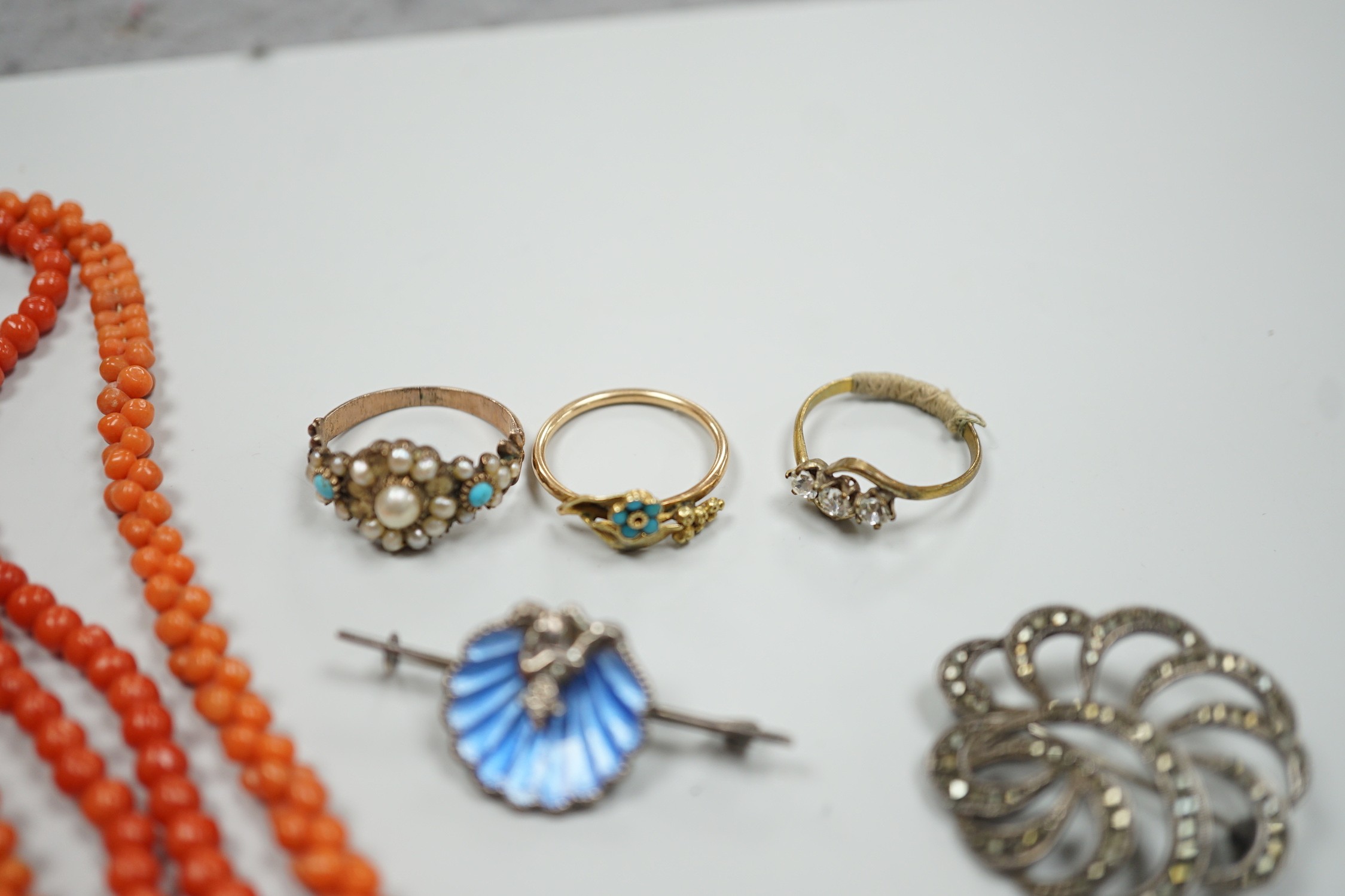 A yellow metal, seed pearl and red stone set 'bird on a branch' brooch, width 30mm, two coral bead necklaces, an enamelled white metal imp and shell brooch, three rings, a marcasite brooch and a simulated pearl necklace.